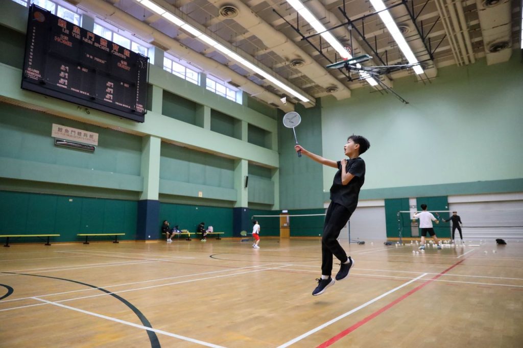 A young athlete in motion playing badminton in a spacious indoor sports facility.
